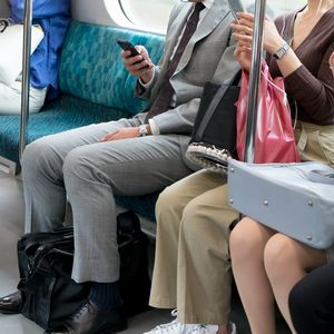 電車内で座席に座ってスマホを見る人々