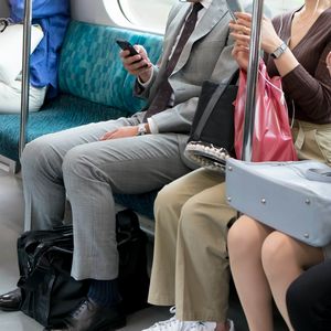 電車内で座席に座ってスマホを見る人々